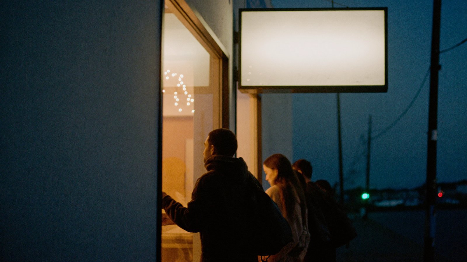 The illuminated marquee of an independent music venue at blue hour with a short line of people waiting at the lit box office window on the sidewalk